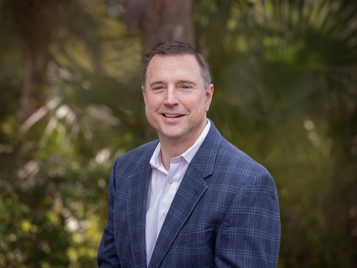 A man in a suit standing next to trees.