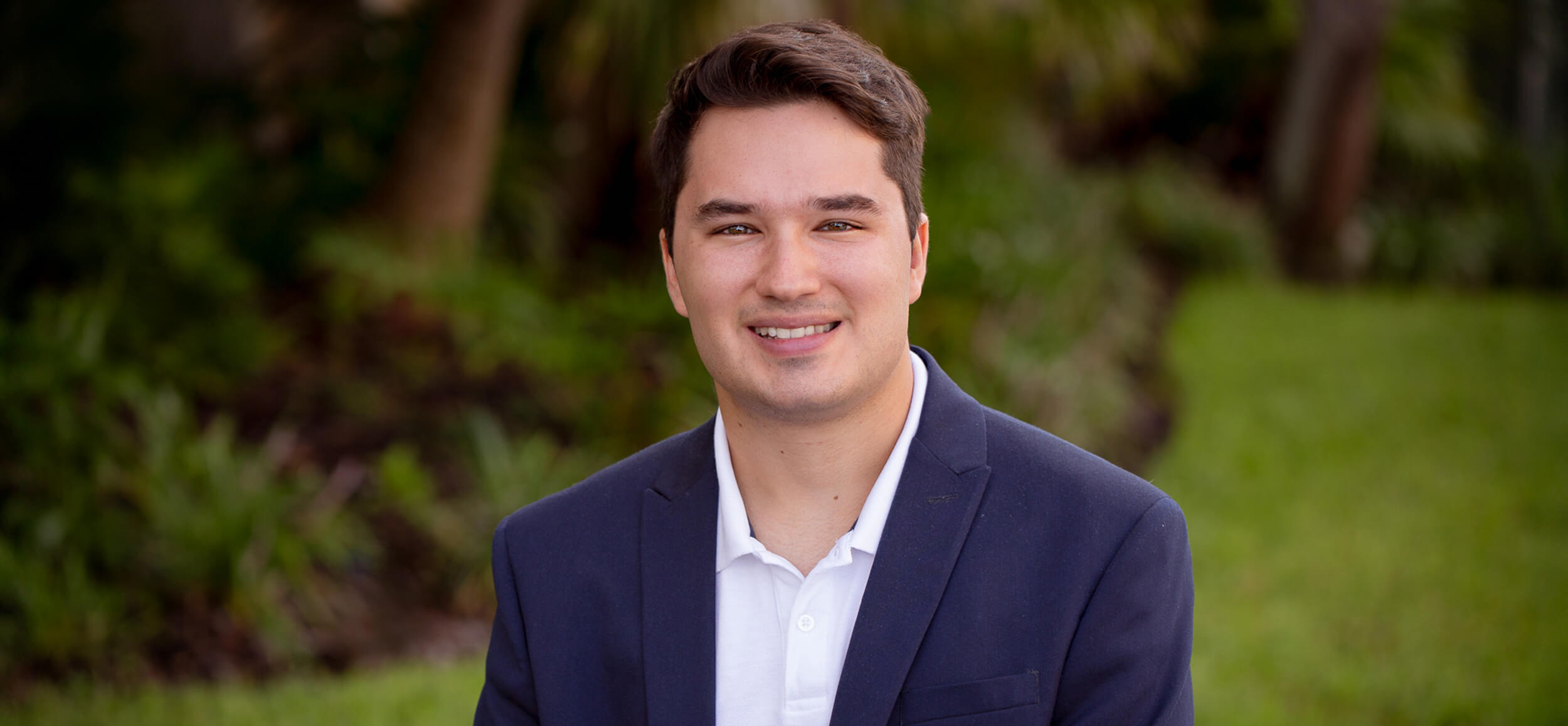 Man smiling outdoors in formal attire.